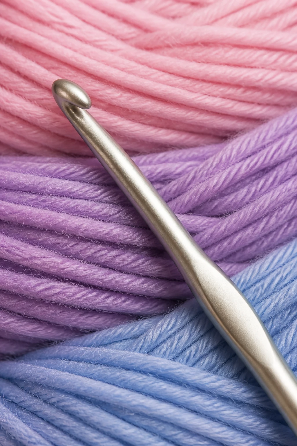 Closeup of a medium crochet hook against soft pastel yarn wound neatly