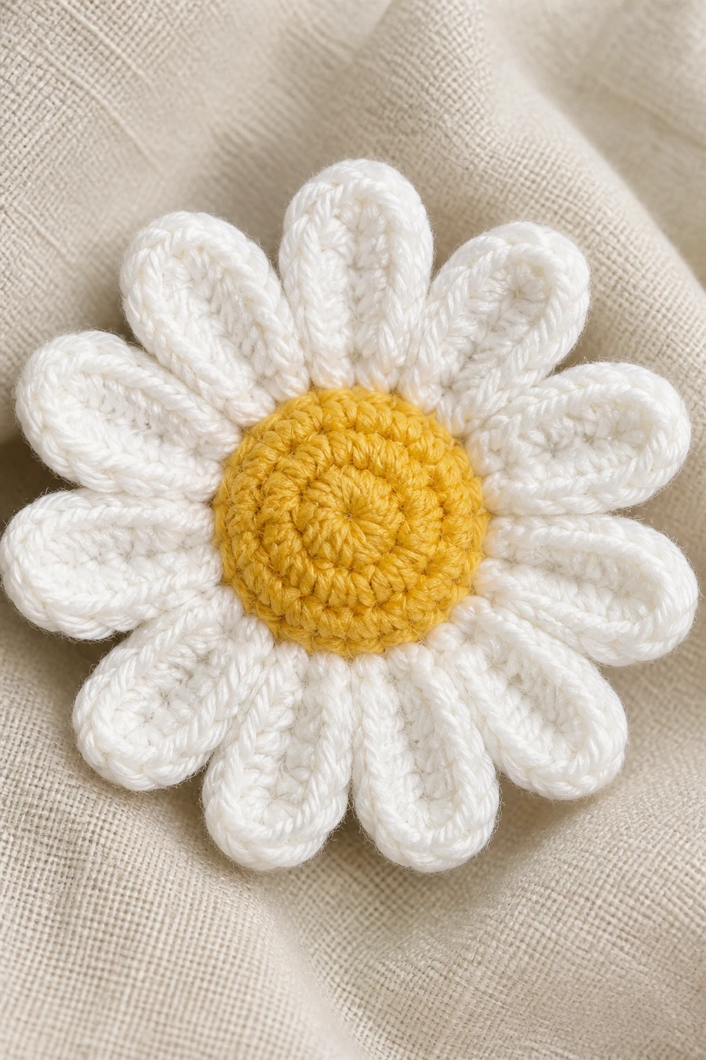 Closeup of a yellow center and white petals crochet daisy on neutral fabric