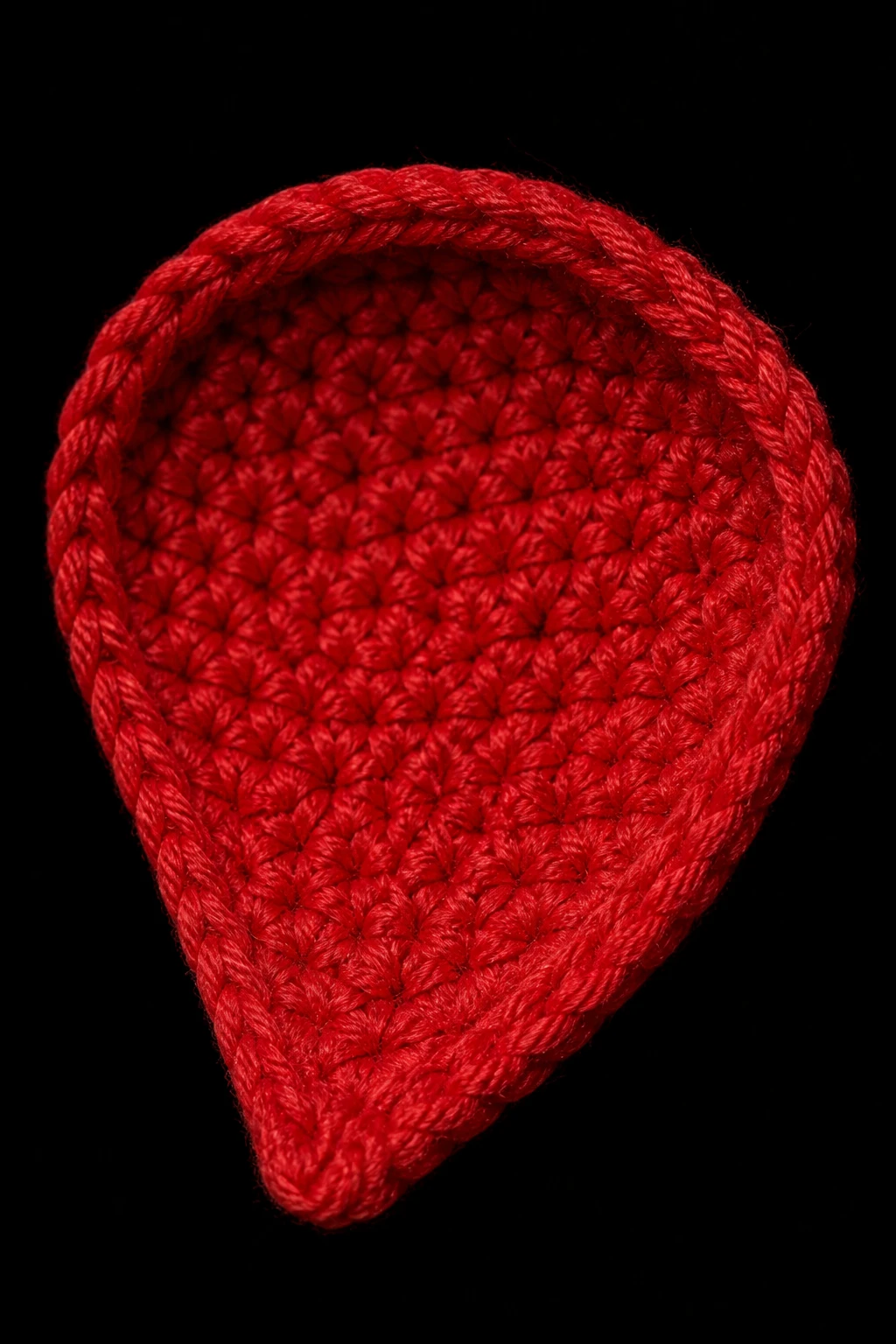 Tight shot of one stiffened crochet rose petal, autofocused texture, plain black studio backdrop