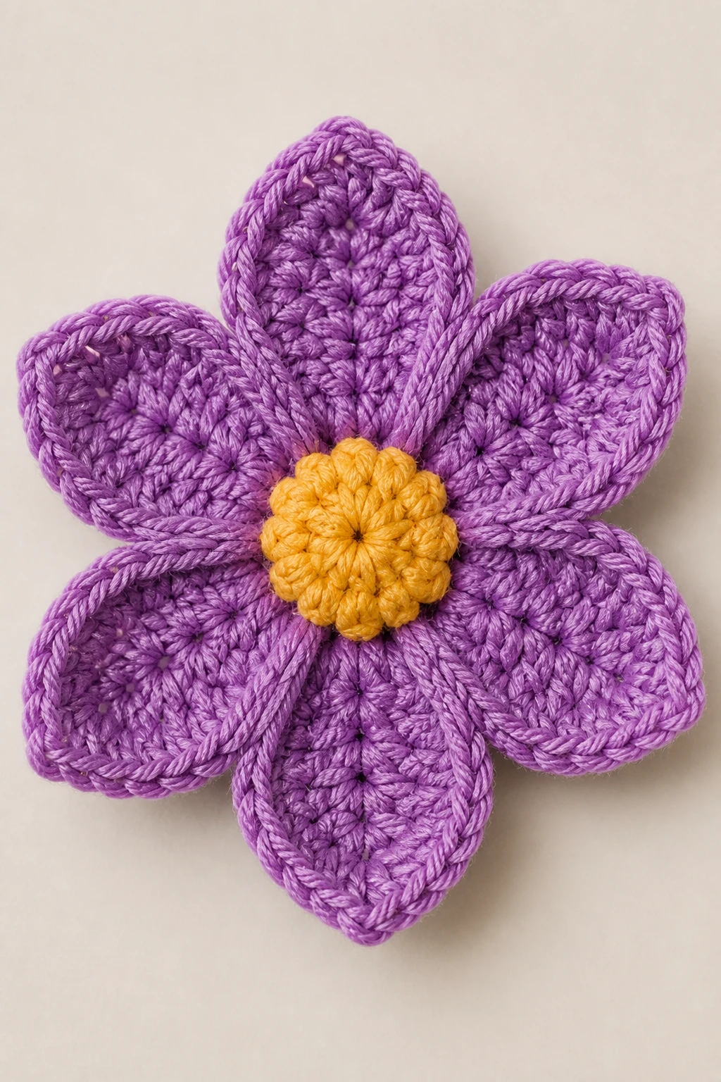 Closeup of a single crocheted flower with crisp petals on a neutral backdrop