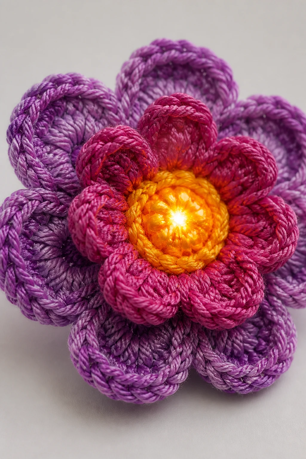 Closeup of a crochet flower with vibrant center gleam against plain studio surface