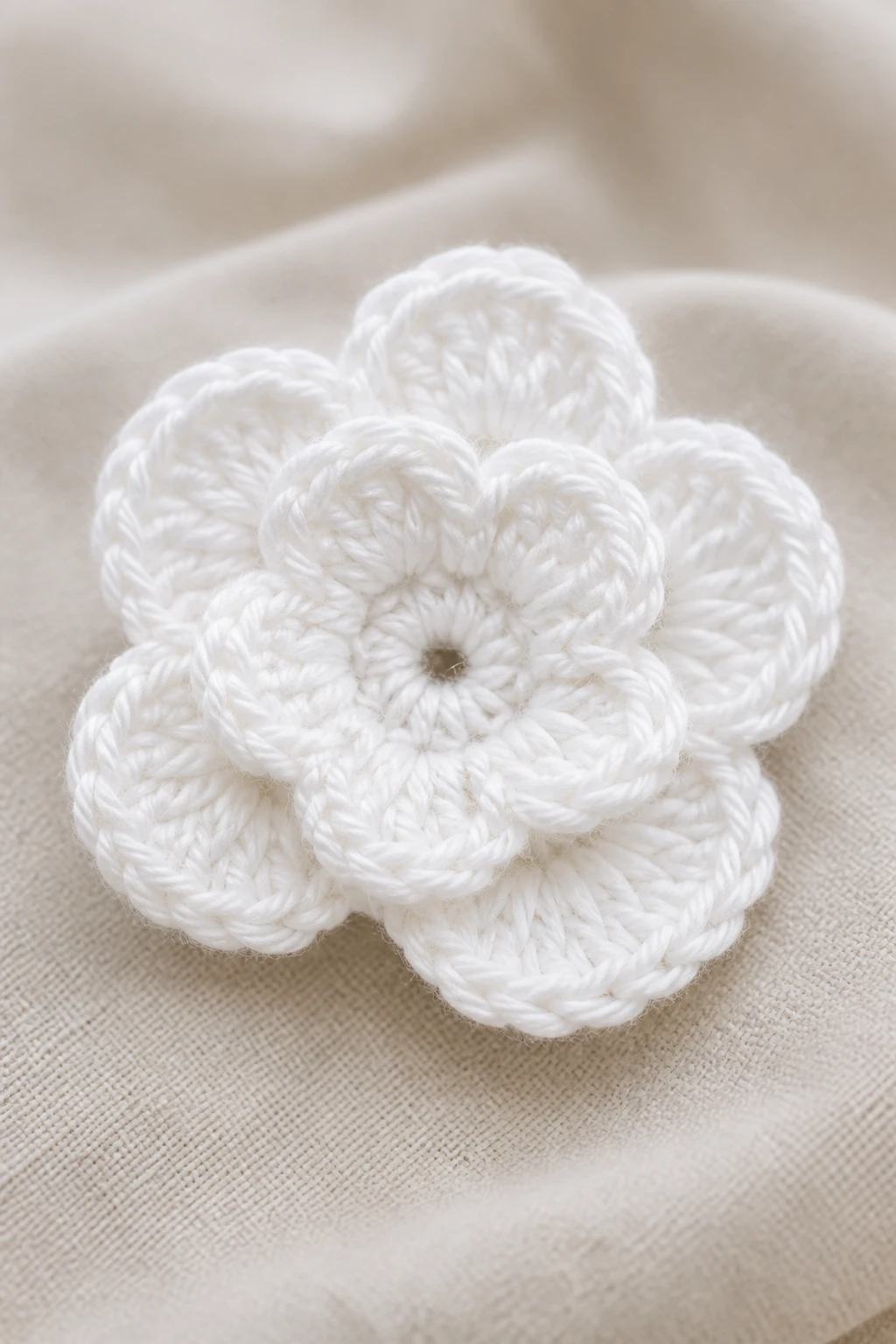 Closeup of a single white crochet flower against a soft neutral fabric backdrop