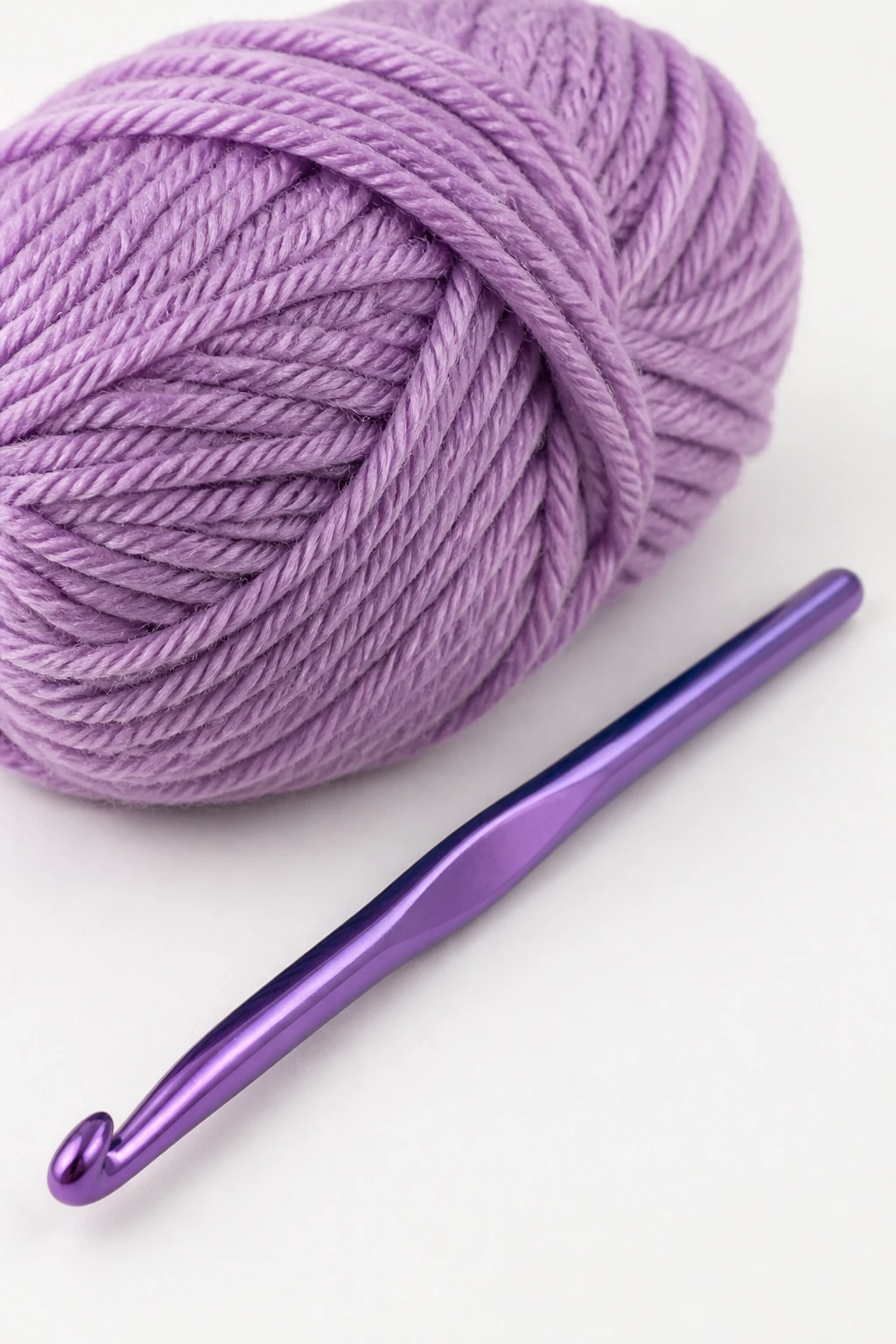 Macro shot of a single crochet hook resting beside a single skein of acrylic yarn on white backdrop