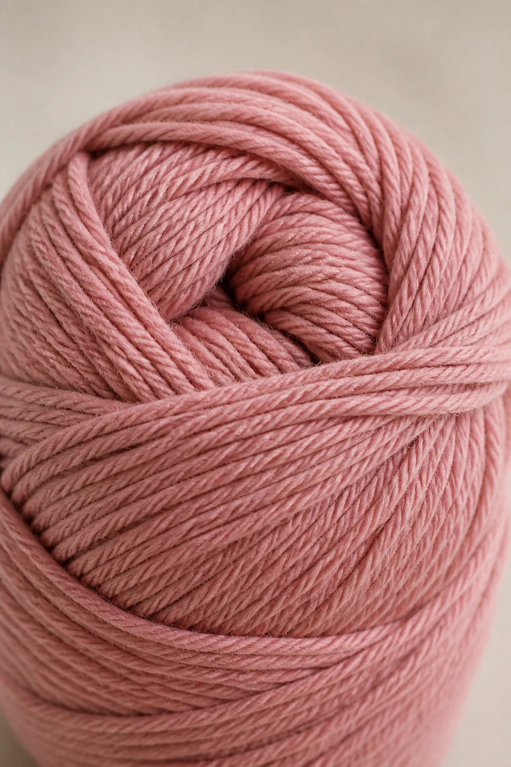 closeup of plush cotton-blend yarn skein in dusty rose on neutral backdrop