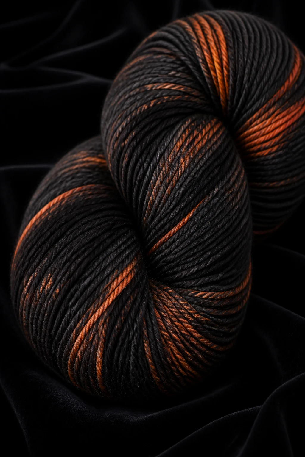 Closeup of black yarn yarn skein with orange accents on dark velvet background